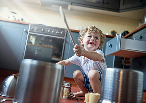 Criança batendo em panelas, enquanto faz música.