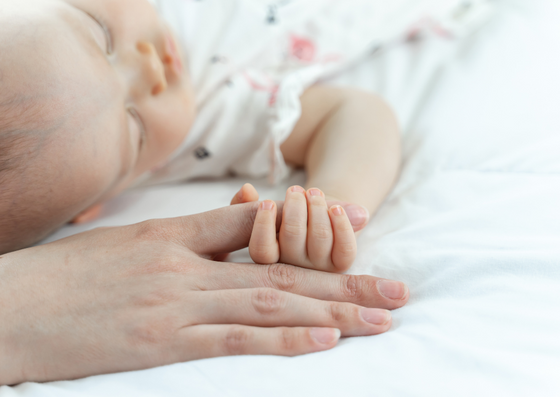 Desenvolvimento do bebê com 6 meses. Bebê deitado na cama, segurando a mão da sua mãe